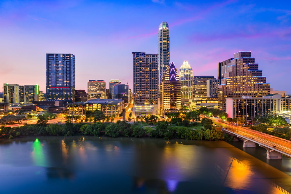 Austin skyline at twilight with illuminated skyscrapers reflected in the Colorado River, surrounded by green trees